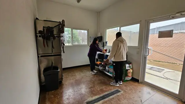 Un cuarto con cabezales y cuerdas colgados en la pared y bultos de alimento, con dos personas trabajando en una mesa de acero
