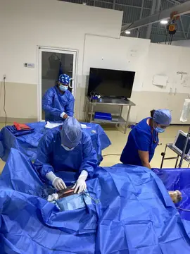 El equipo quirúrgico, con bata, gorro y cubrebocas, operando bajo campos azules