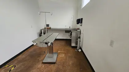 Una sala de paredes blancas con una mesa de exploración de acero inoxidable, porta sueros y tanque de oxígeno
